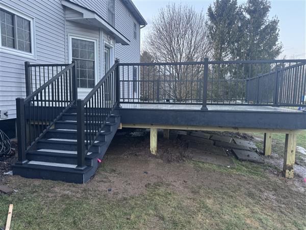 Back deck with black stairs and railing beside a gray house, raised on posts over a grassy yard
