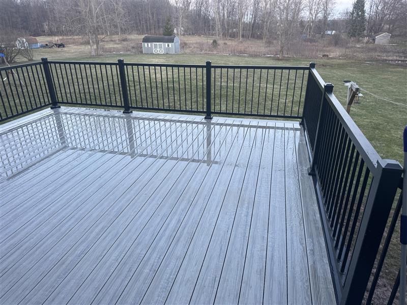 Wet gray deck with black railing overlooking a grassy backyard and trees