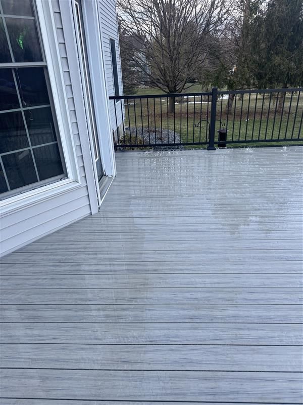 Wet gray deck beside house with black railing and trees beyond