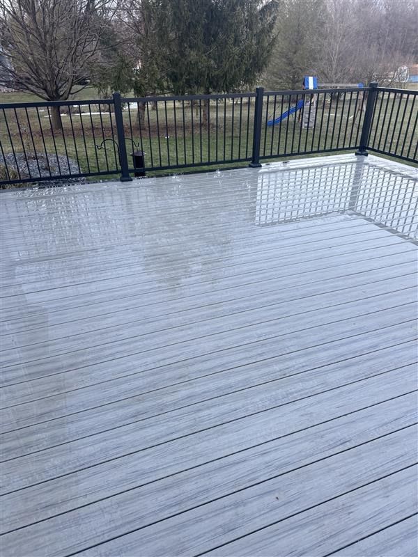 Wet gray deck with black railing overlooking bare trees and a yard
