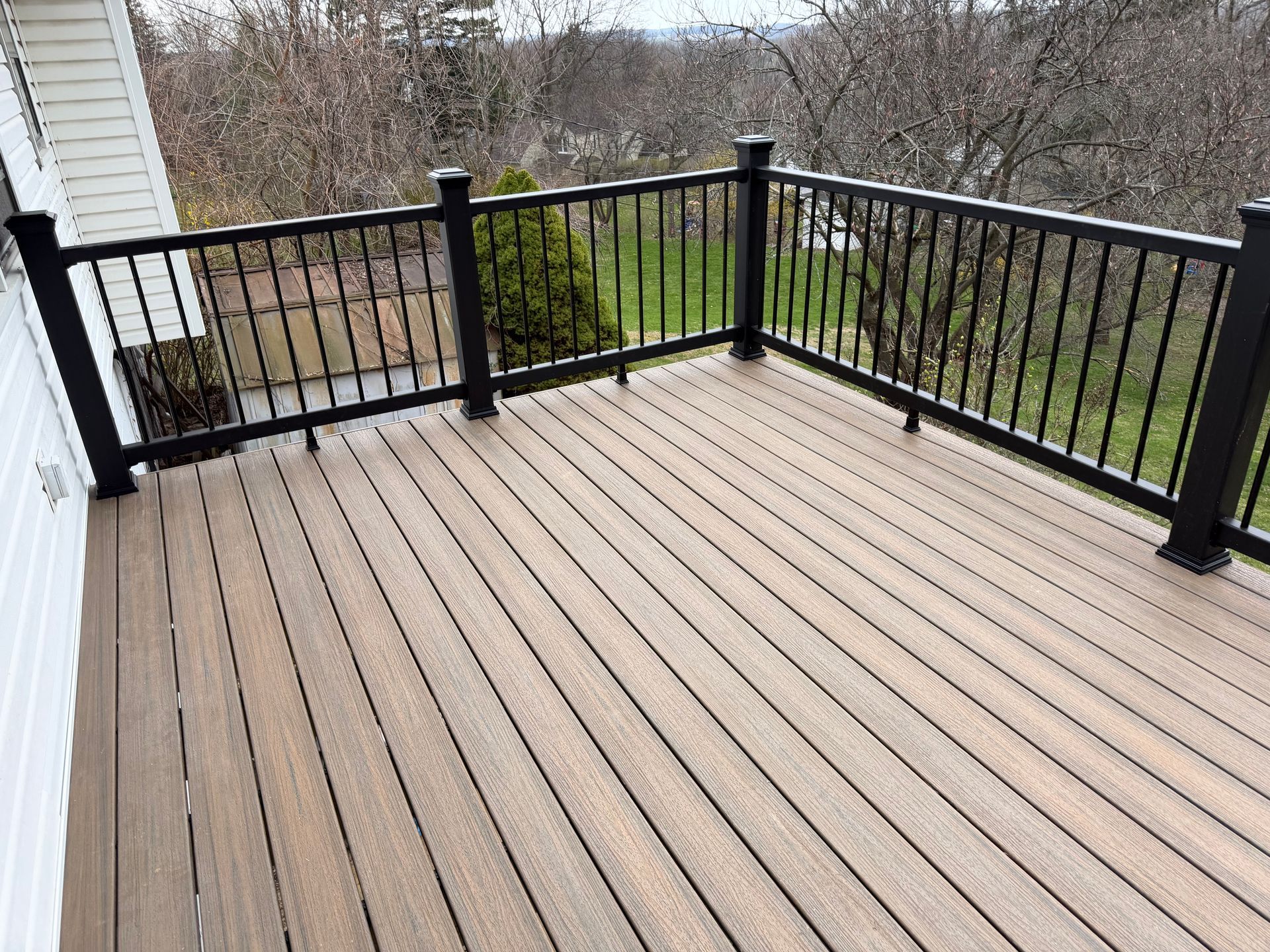 Wooden deck with black railings overlooking a backyard and trees
