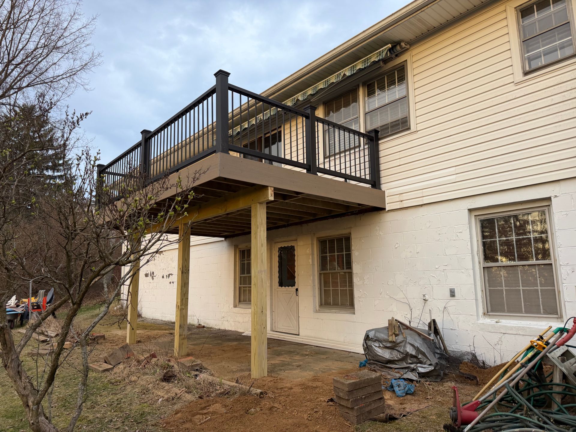 Two-story house exterior with a raised black deck and cluttered yard below