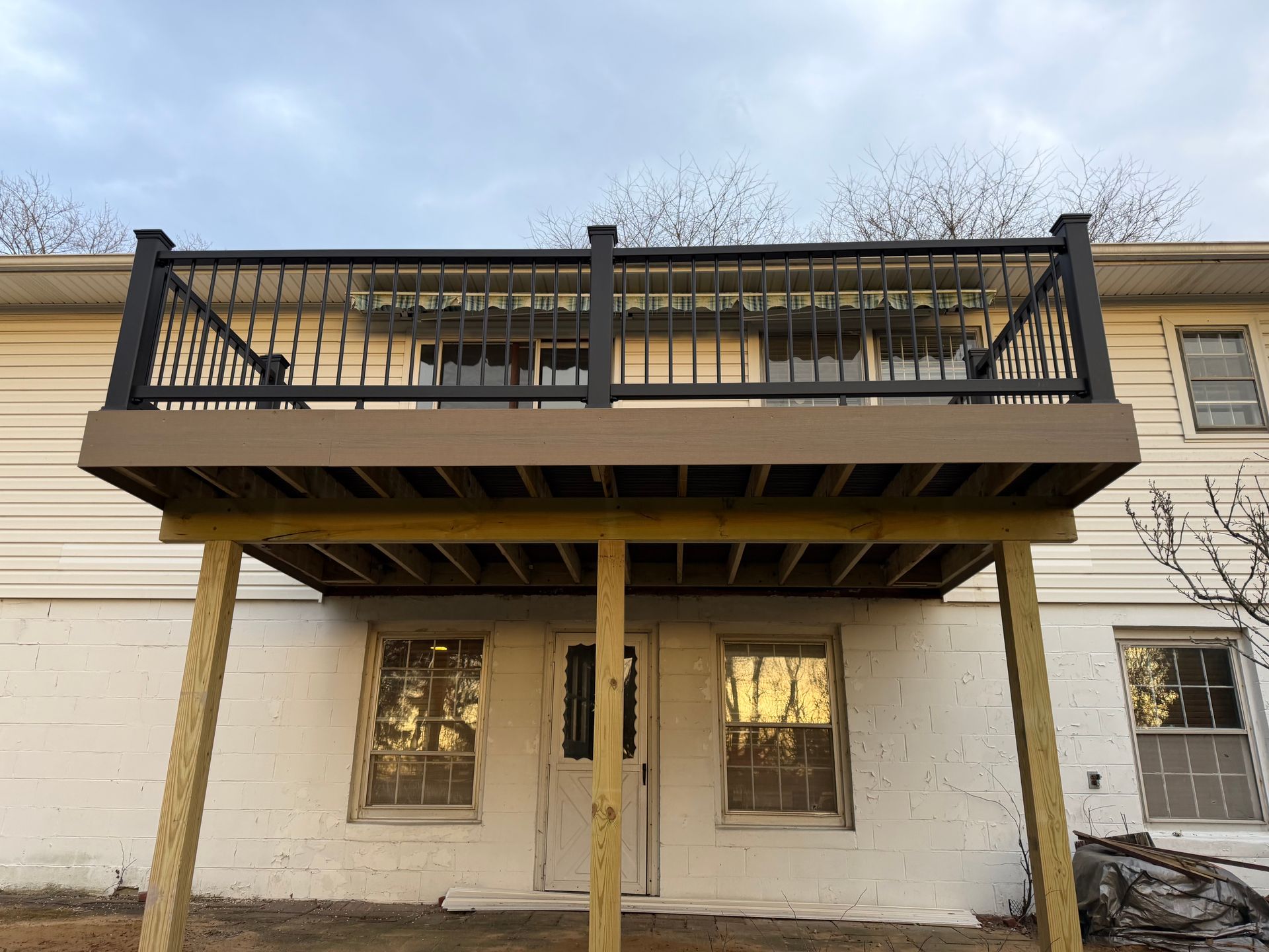 Back deck on a beige house with black railings and stairs above a covered patio