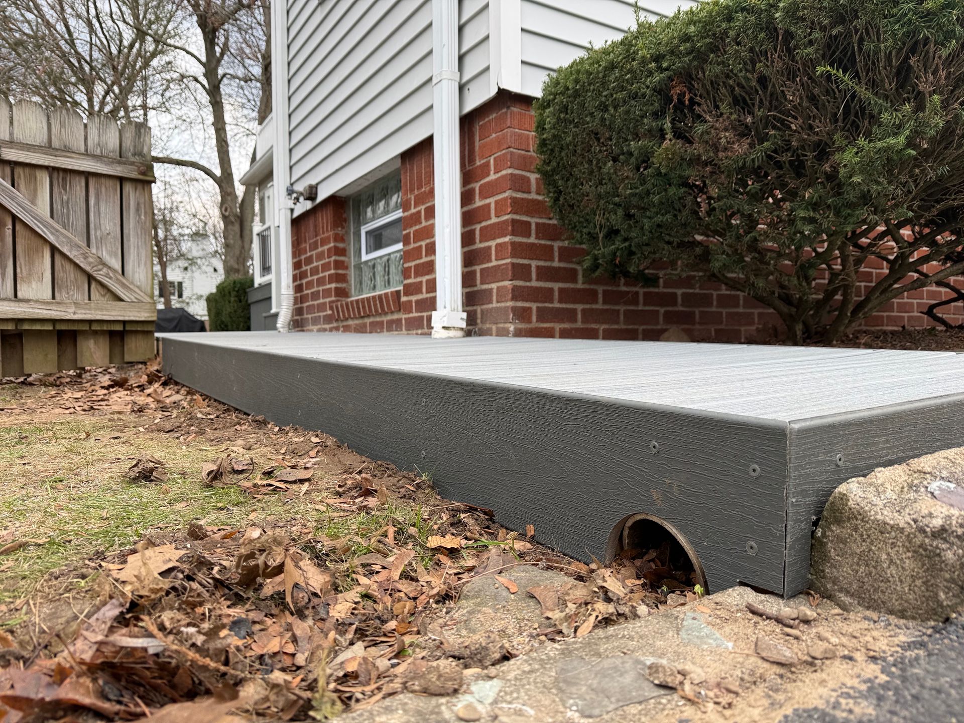 Raised gray concrete slab beside a brick house with a small drainage opening near the ground