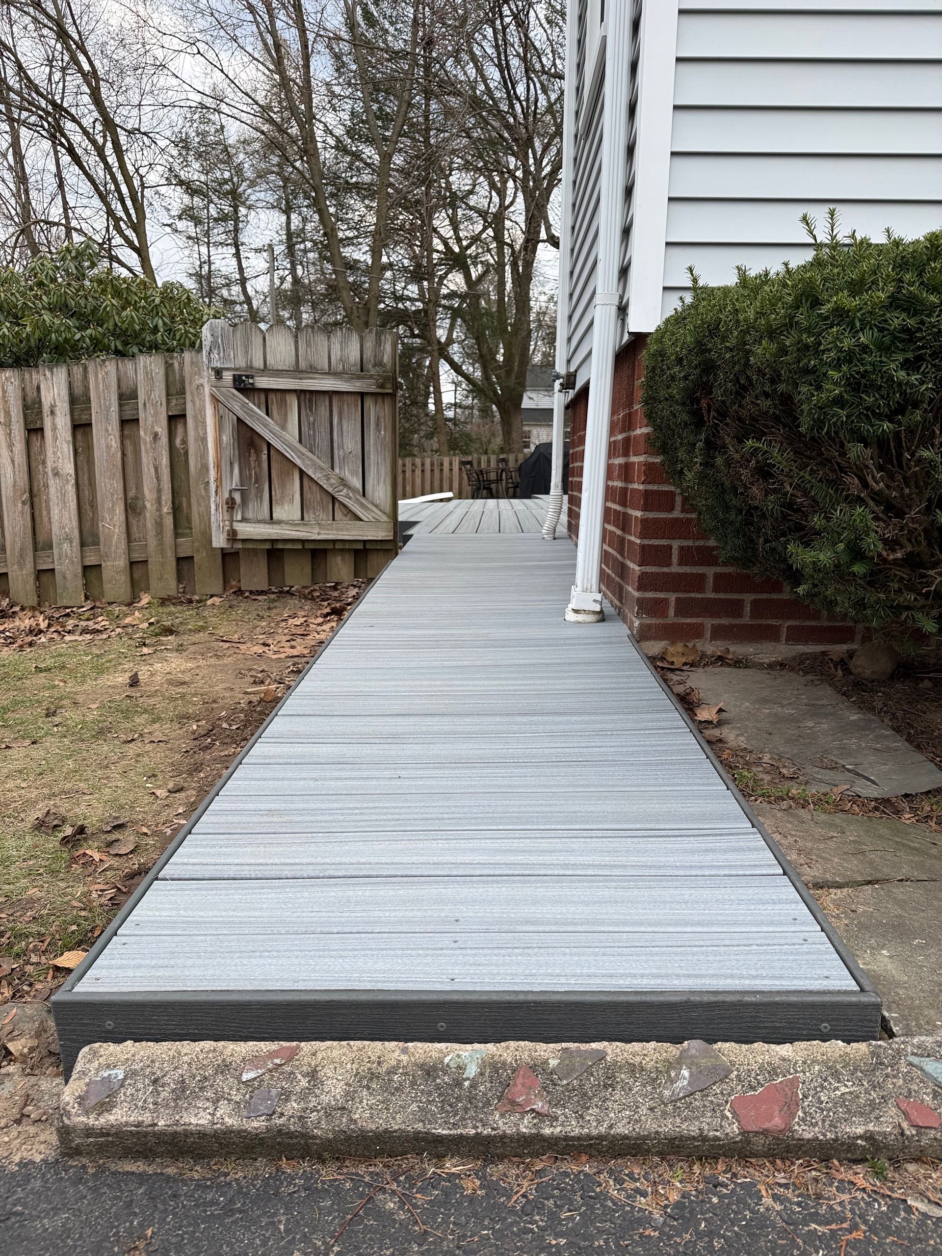 Concrete wheelchair ramp beside a house, leading up from a stone step to a side door fenced yard.