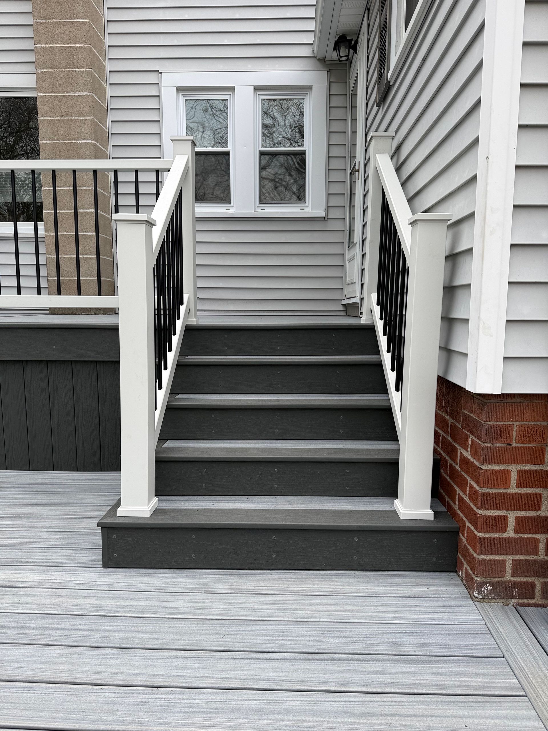 Front steps with gray stairs, white railings, and brick siding leading to a house entrance.