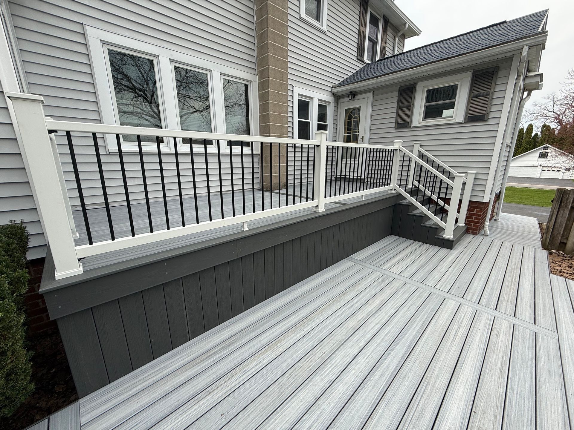 Gray deck with white railings and steps beside a house, featuring dark gray skirting and composite flooring.
