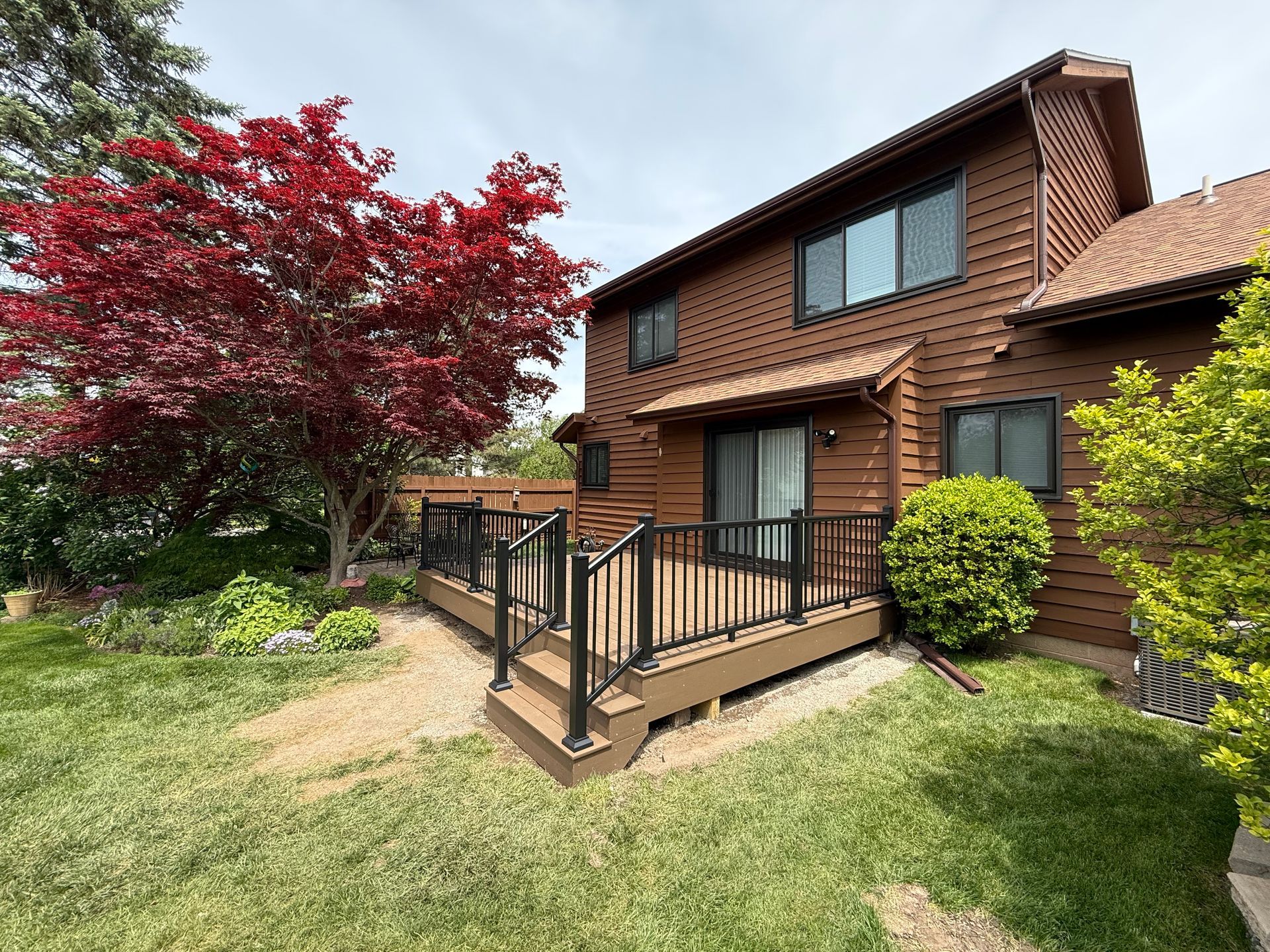 Two-story brick house with a small porch, green lawn, and a red-leaf tree in the front yard