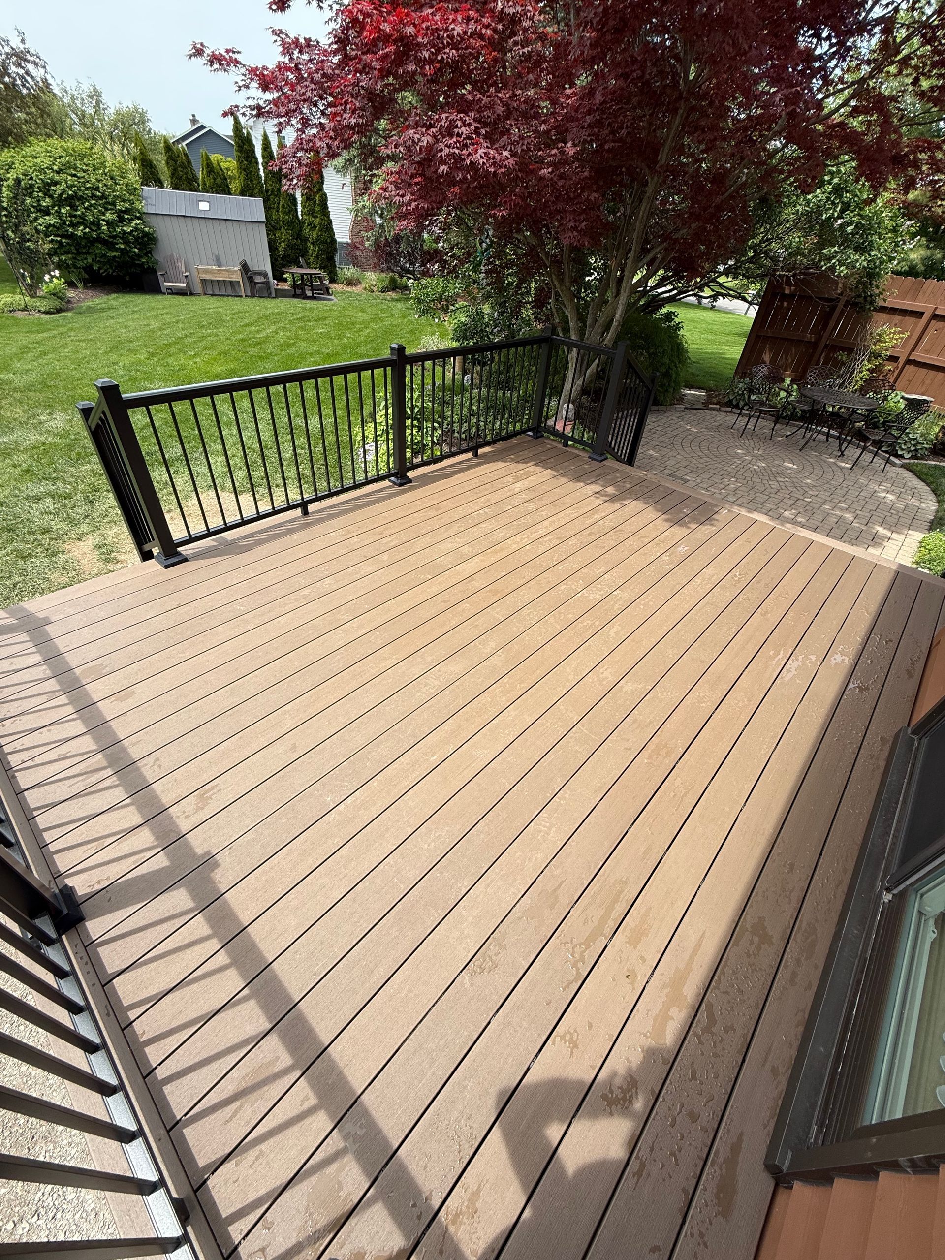Wooden deck with black railing, potted tree, and garden lawn in a sunny backyard