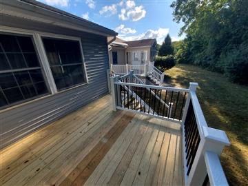 A new wooden deck attached to a gray house, featuring white railings with black spindles and stairs leading to the yard.