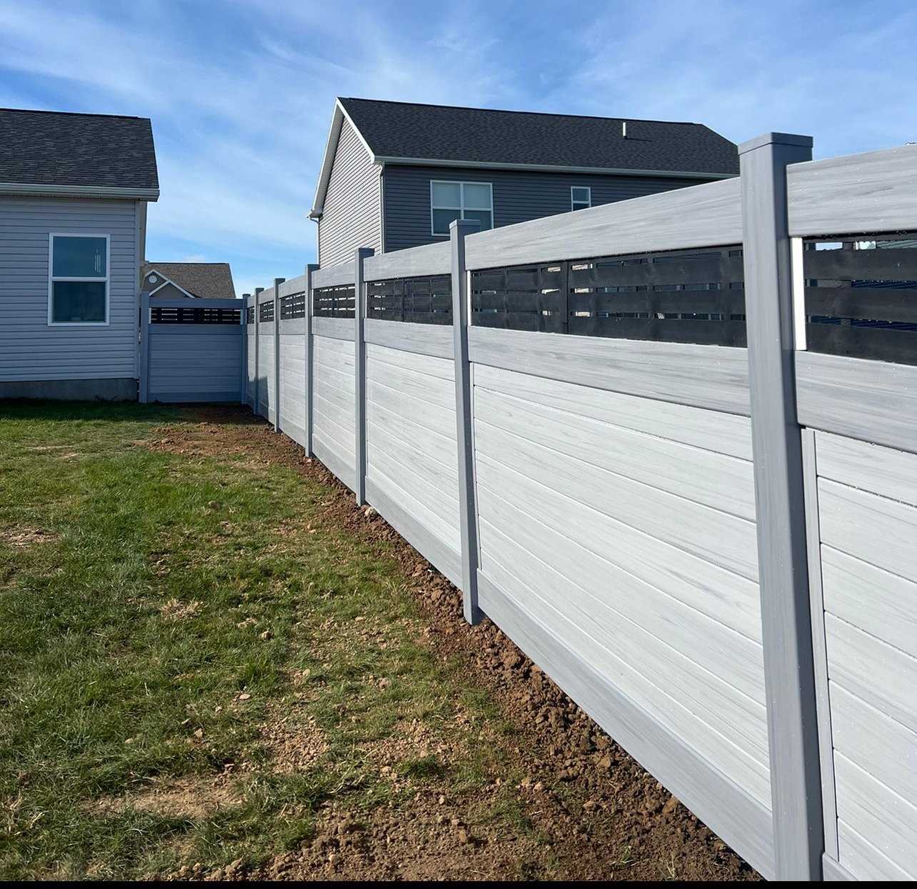 A light gray vinyl privacy fence with a decorative black lattice topper runs along the side of a grassy residential yard.