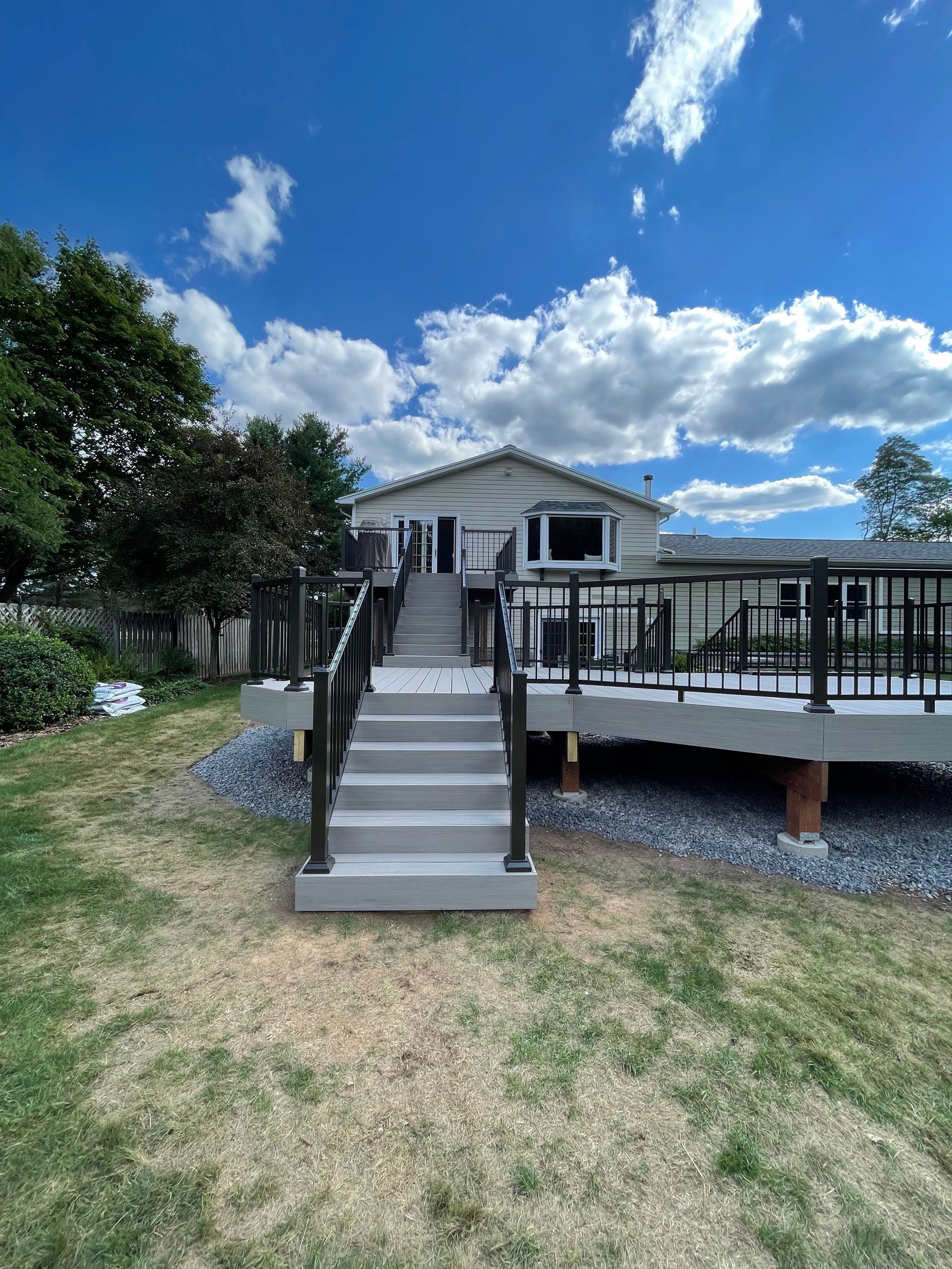 Grey deck with stairs leading up to a house with a blue sky and clouds.