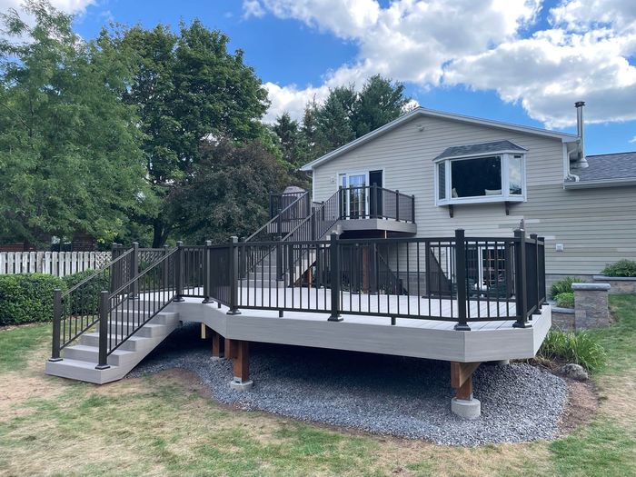 Gray deck with black railing and steps attached to a light-colored house.