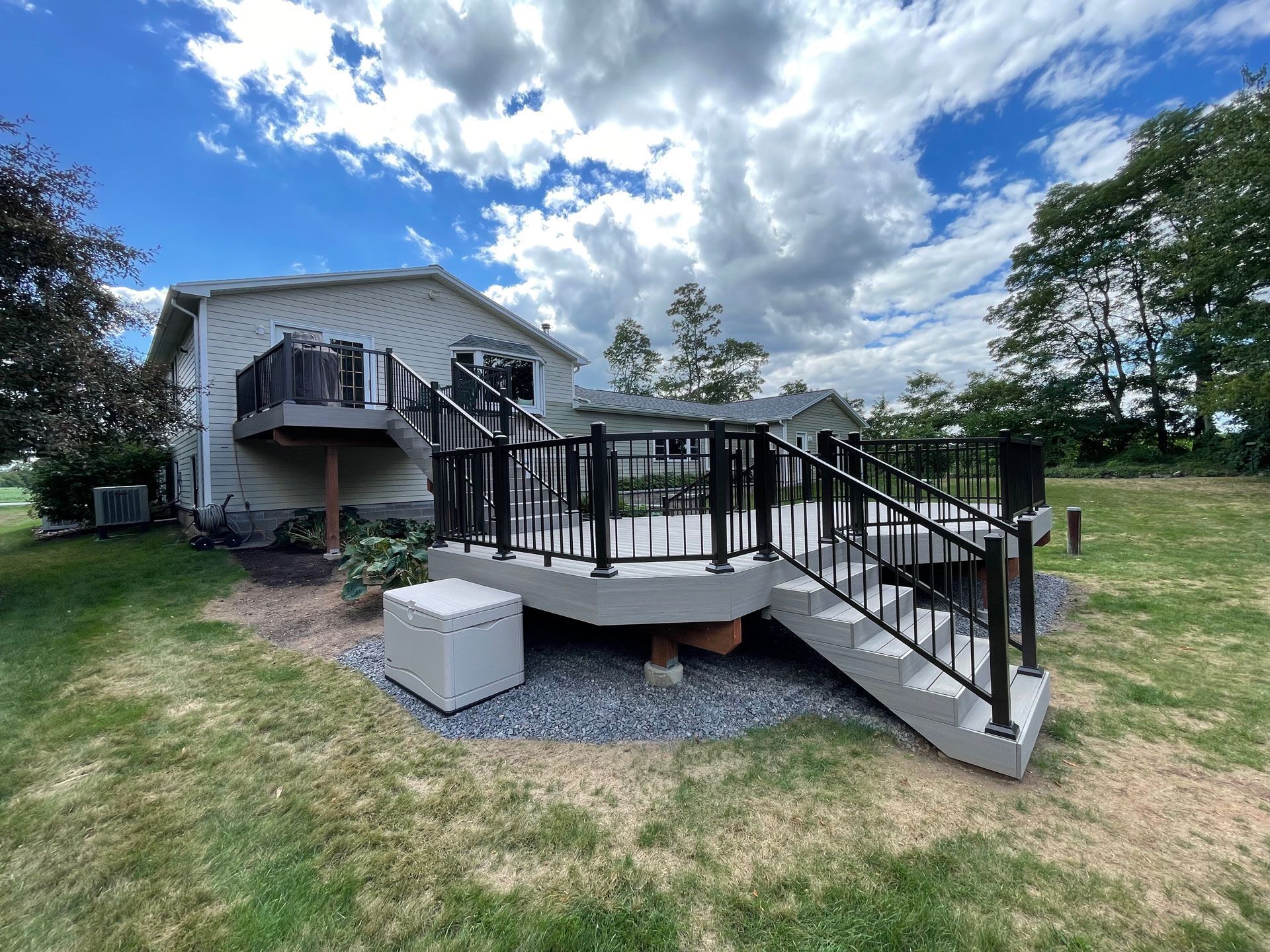 Backyard deck with black railings and gray steps, against a cloudy blue sky.