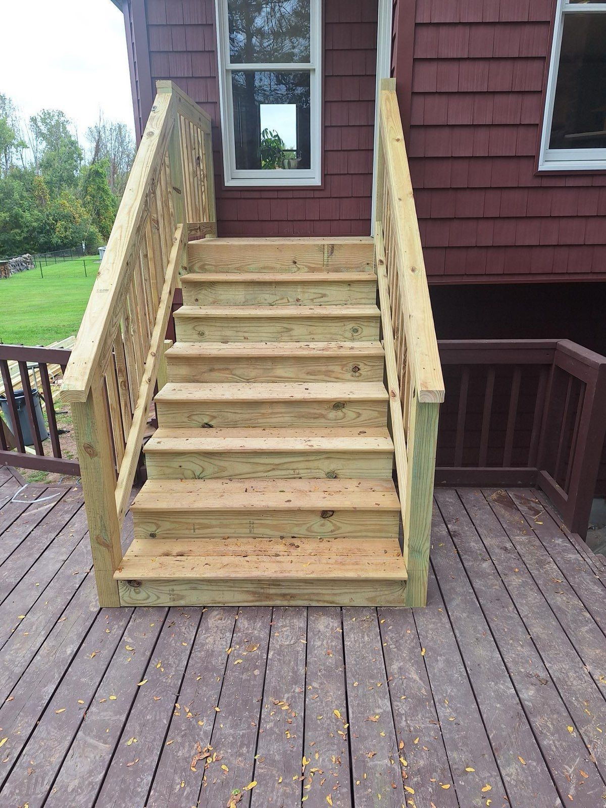 Wooden outdoor stairs leading up to a red-sided house with a deck.