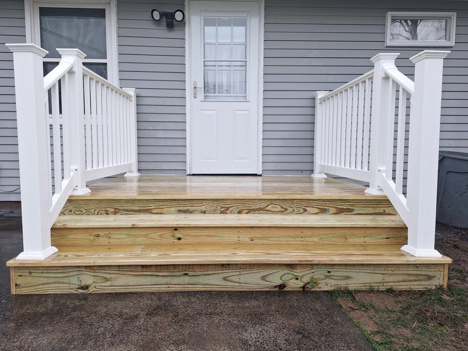 Wooden porch with white railings and steps leading to a white door.