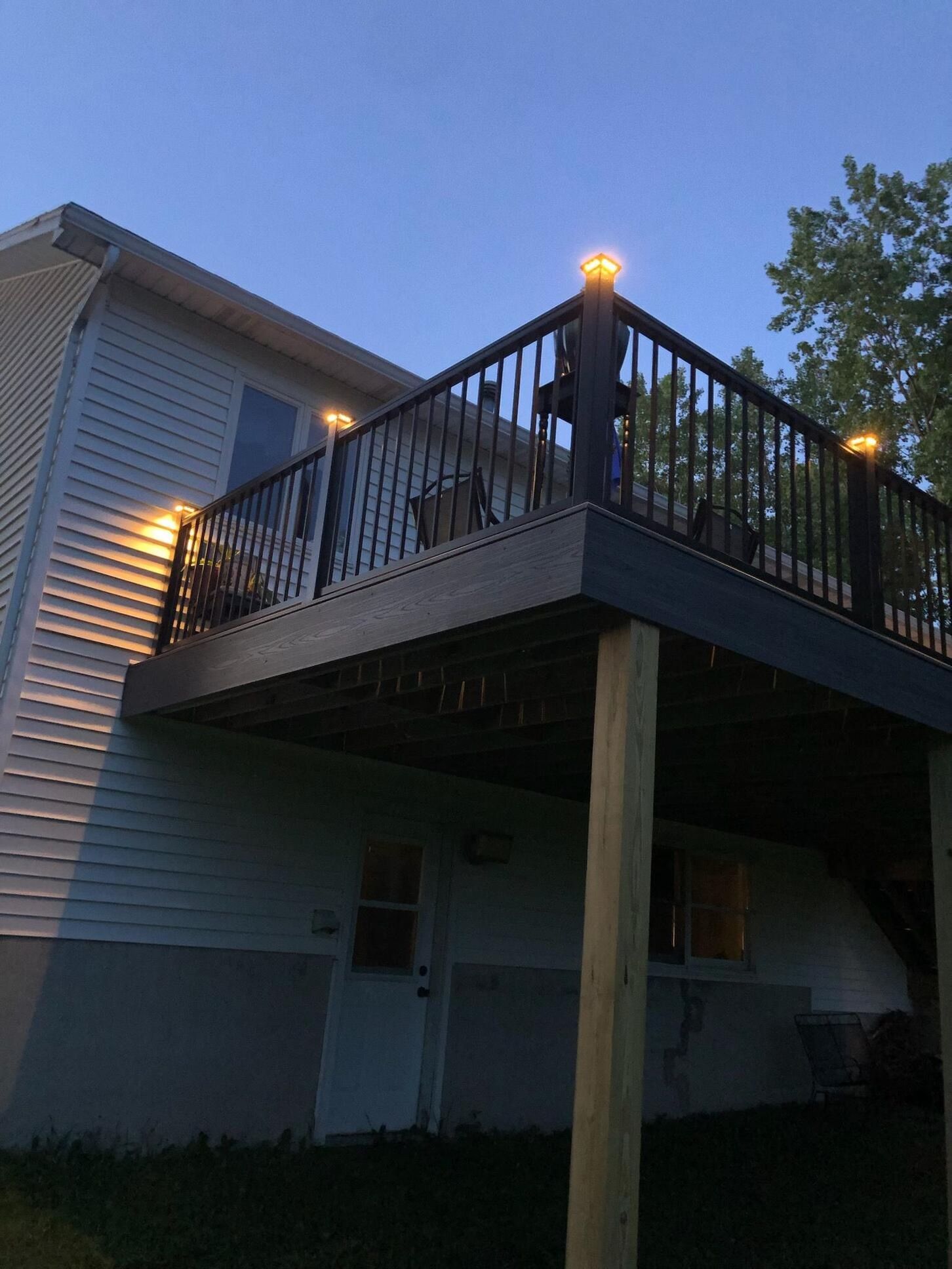 Deck with lit post lights, attached to a white house, at dusk.