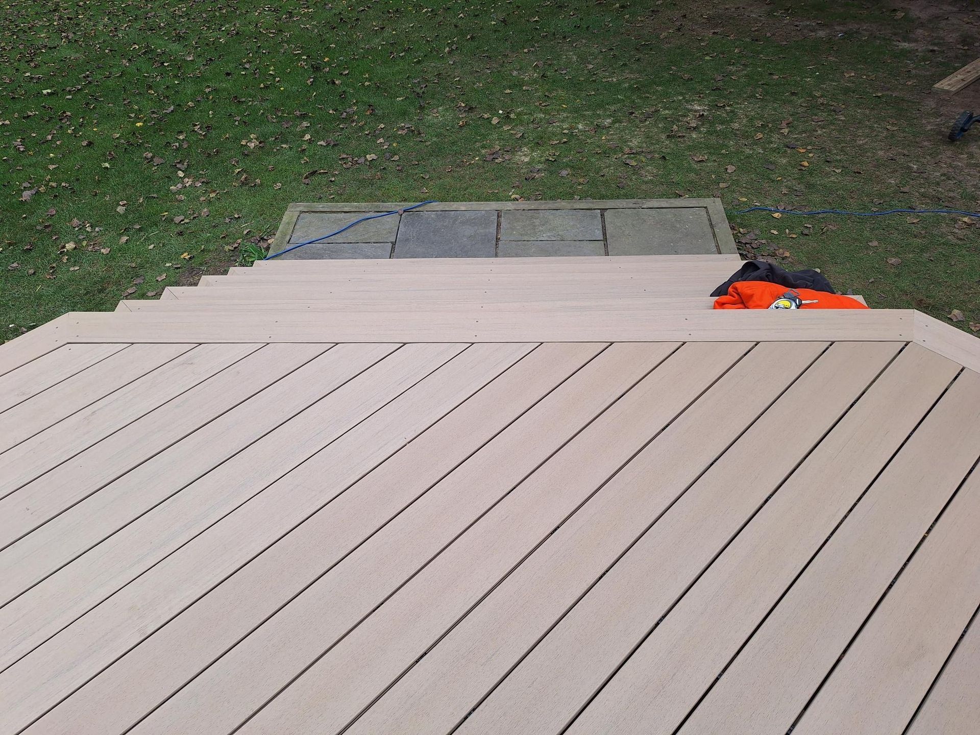 Beige composite deck with steps leading to a gray surface and grass background.
