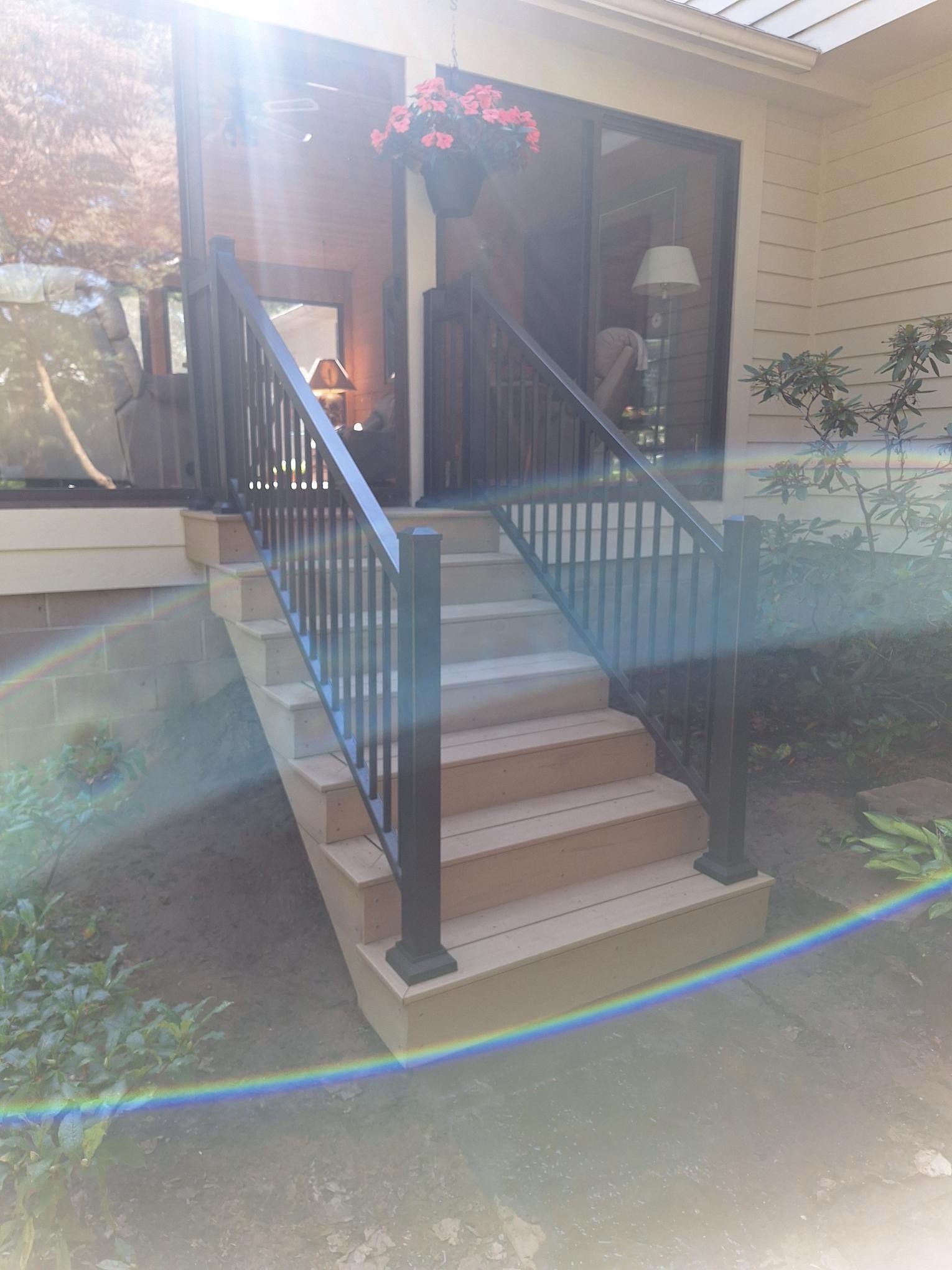 Exterior stairs leading up to a building's entrance. Black railings and tan stairs. Sunlight flares.
