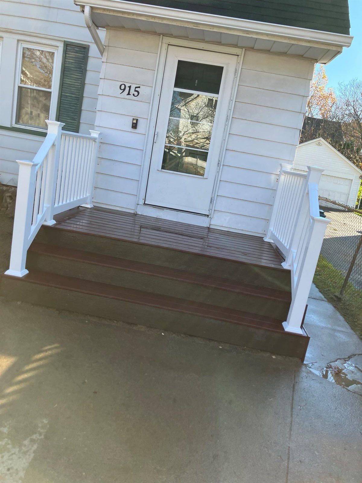 A white house with a front porch and stairs, featuring white railings and a dark brown deck.