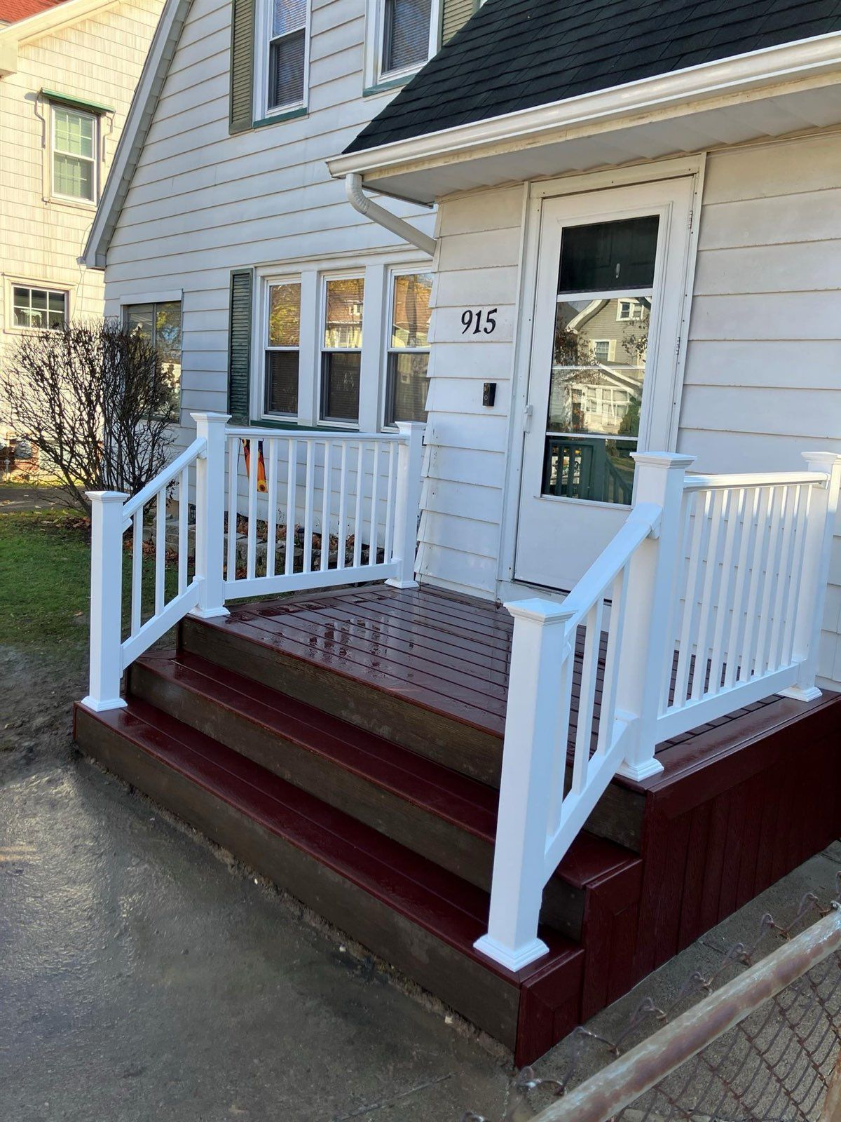 White porch with stairs leading to a white door on a house, with white railing.