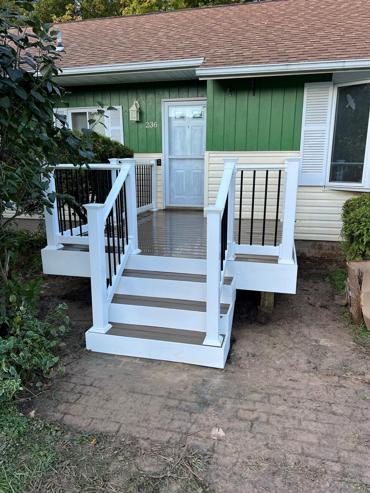 White steps and porch with black railing leading to a green house entrance.
