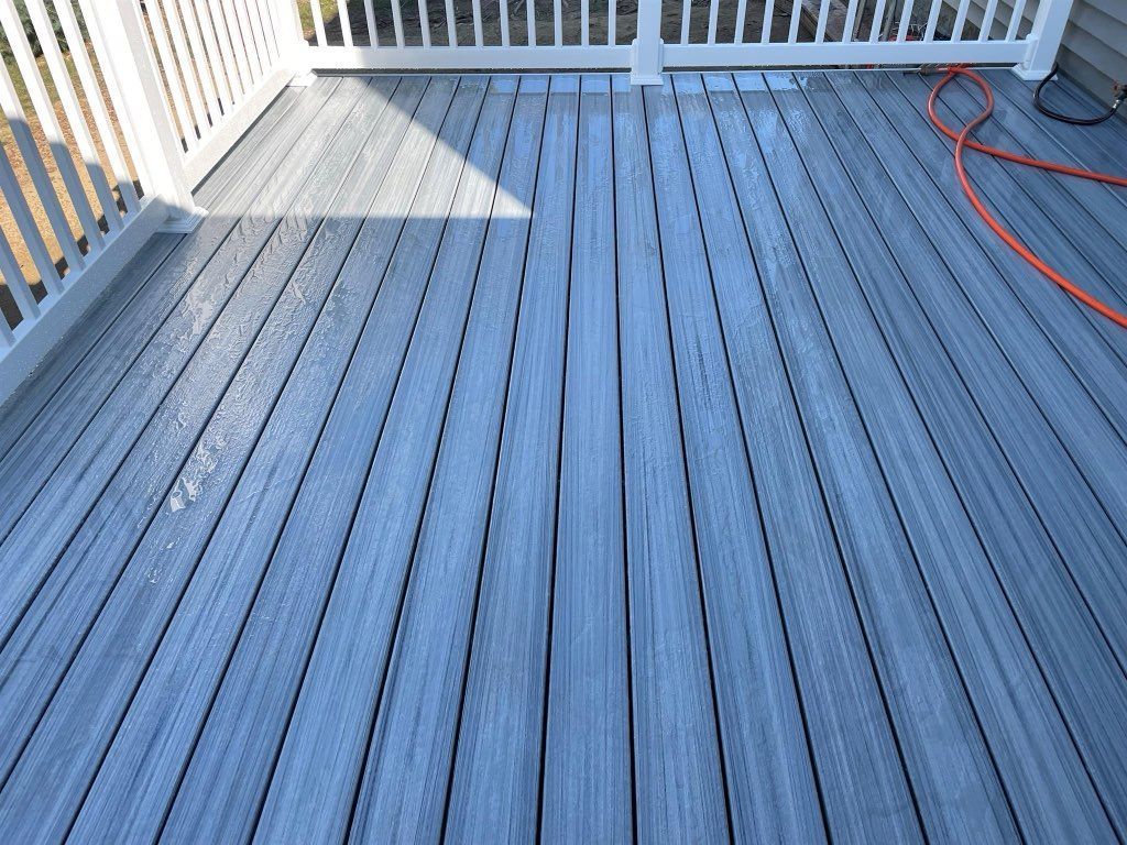 Gray composite deck with white railing, an orange hose, and sunshine.