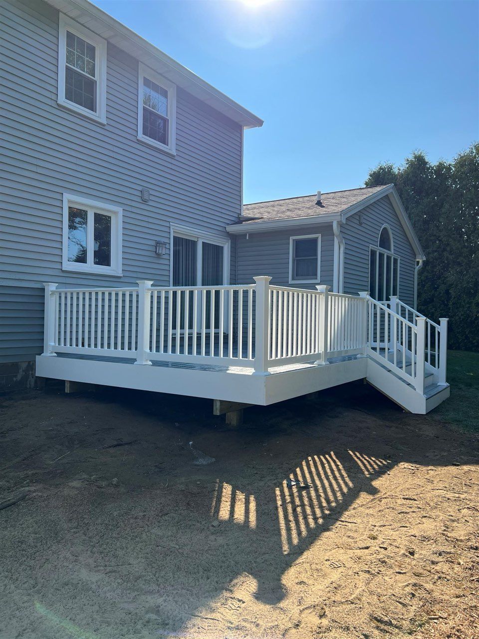 White deck with railings attached to a two-story house, with a bright sunny sky.