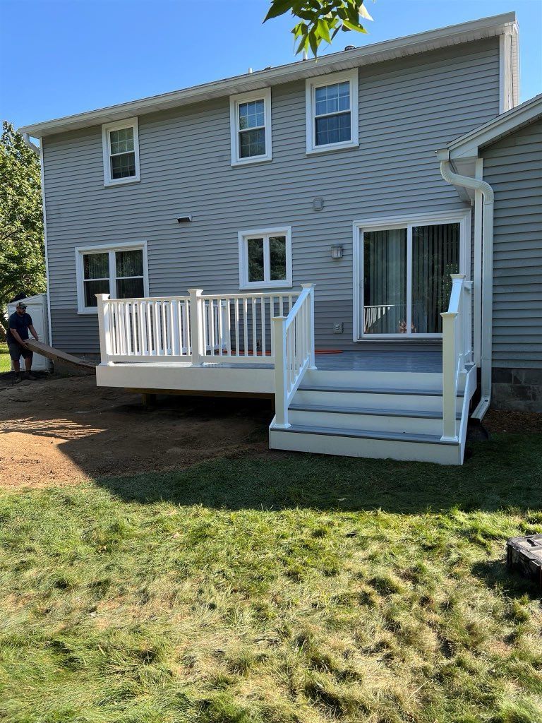 Backyard with a new deck attached to a two-story gray house; stairs lead down to the lawn.