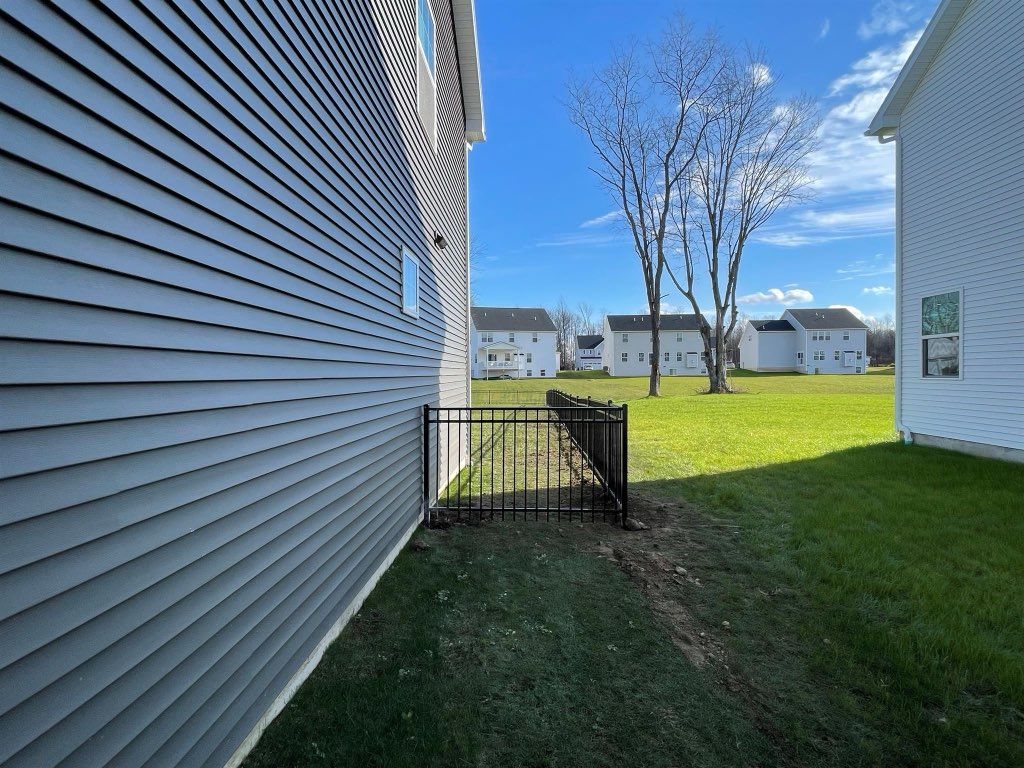 Gray house siding next to a small black fence and grassy yard. Blue sky, other houses visible.