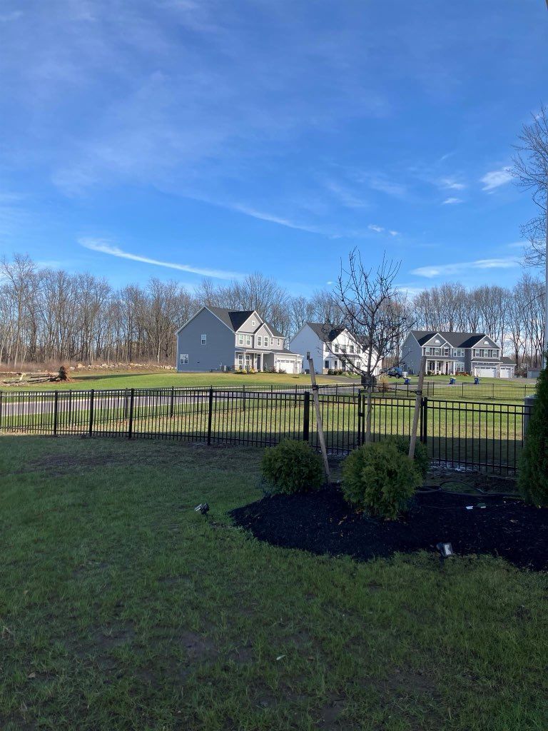 View of houses across a pond and black fence. Bright blue sky.