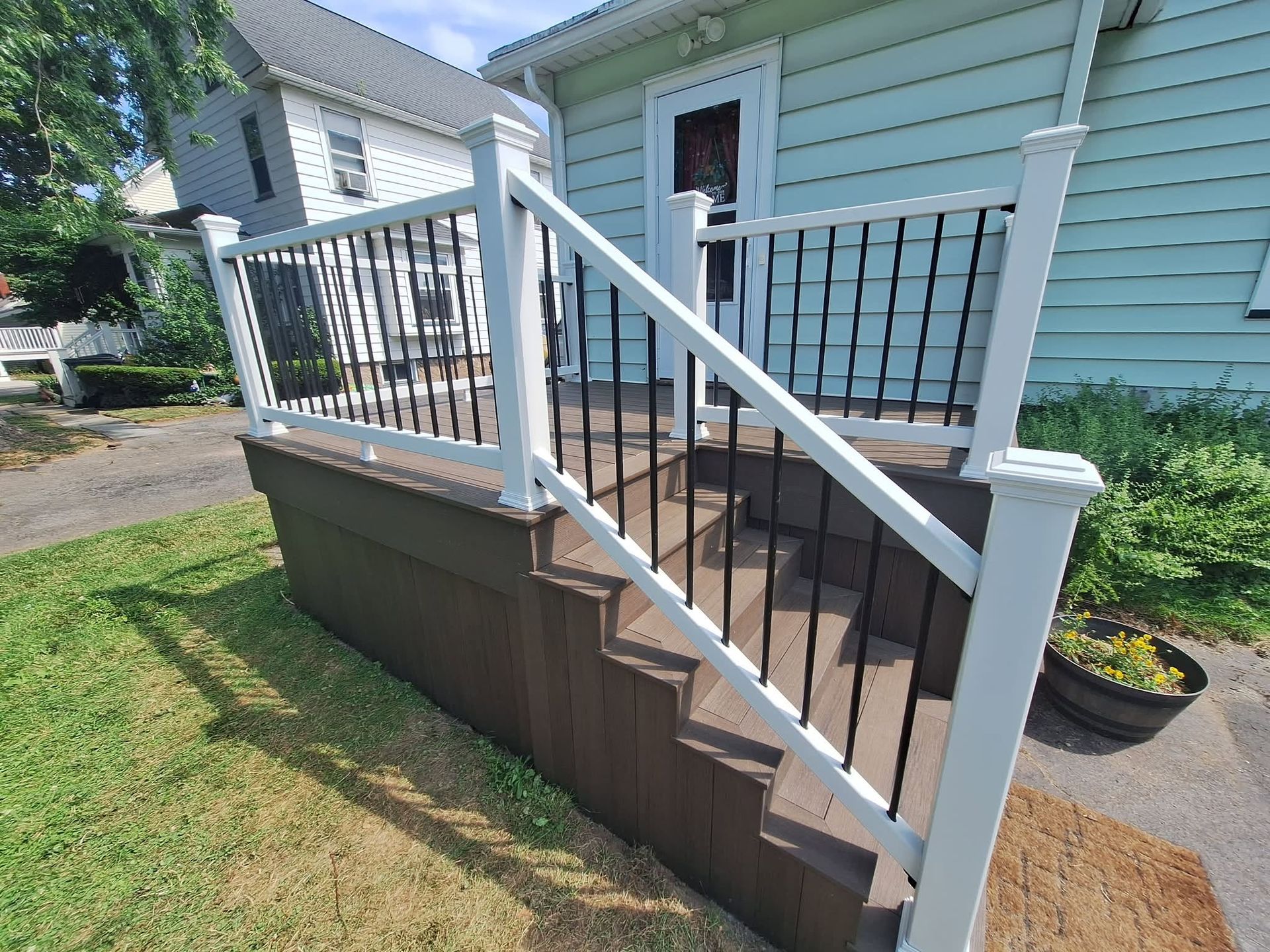 Front porch stairs with black railings and a brown skirt on a light blue house