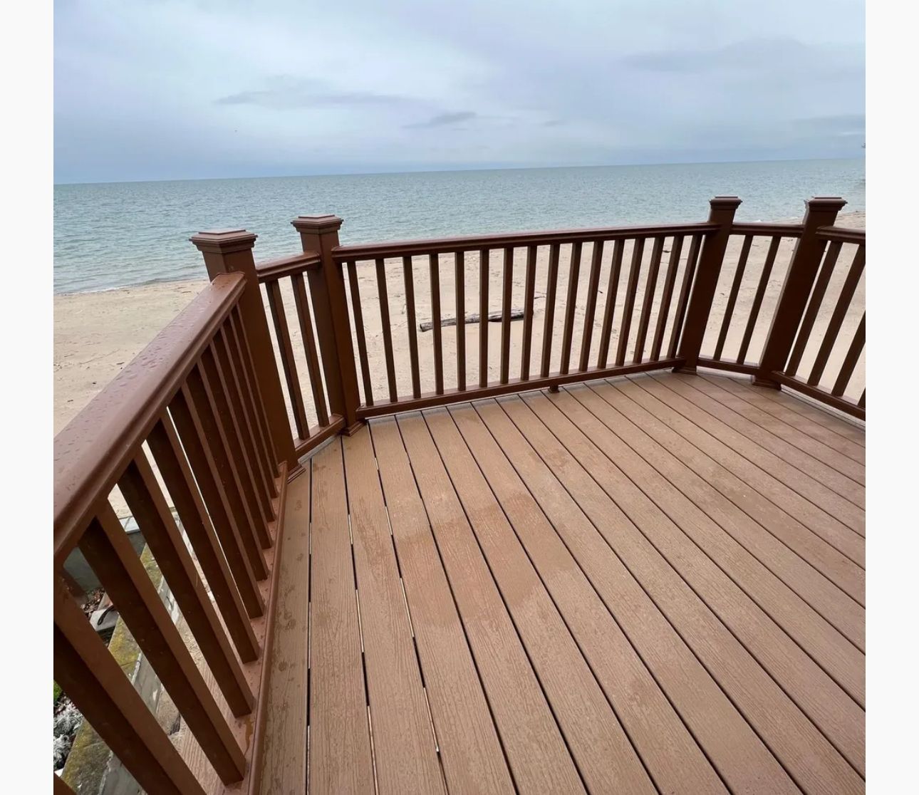 Wooden deck overlooking a sandy beach and calm ocean under a cloudy sky