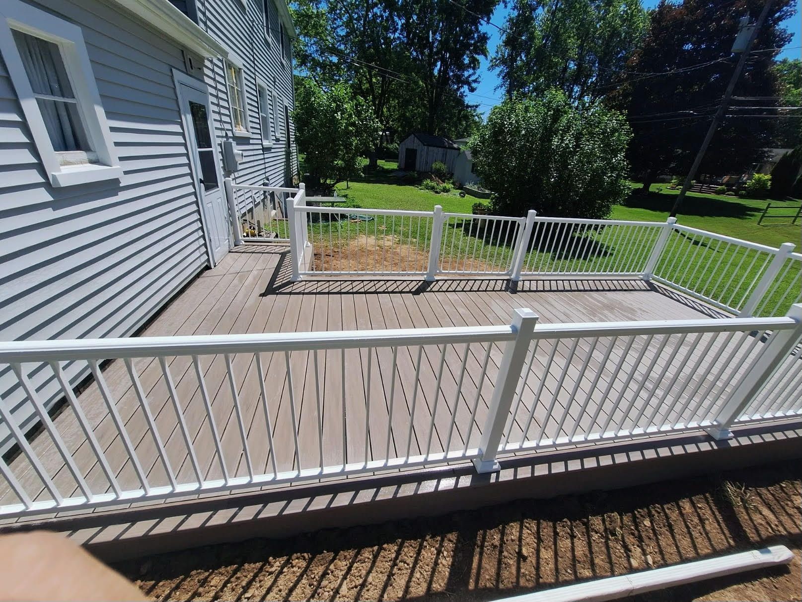 A white fence surrounds a wooden deck in front of a house.