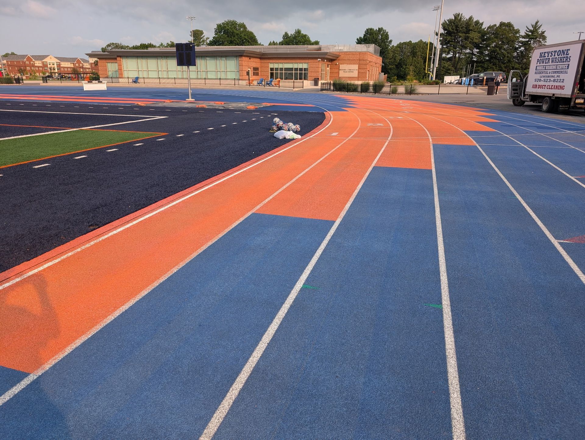 Blue and orange running track curving around a school athletic field under an overcast sky