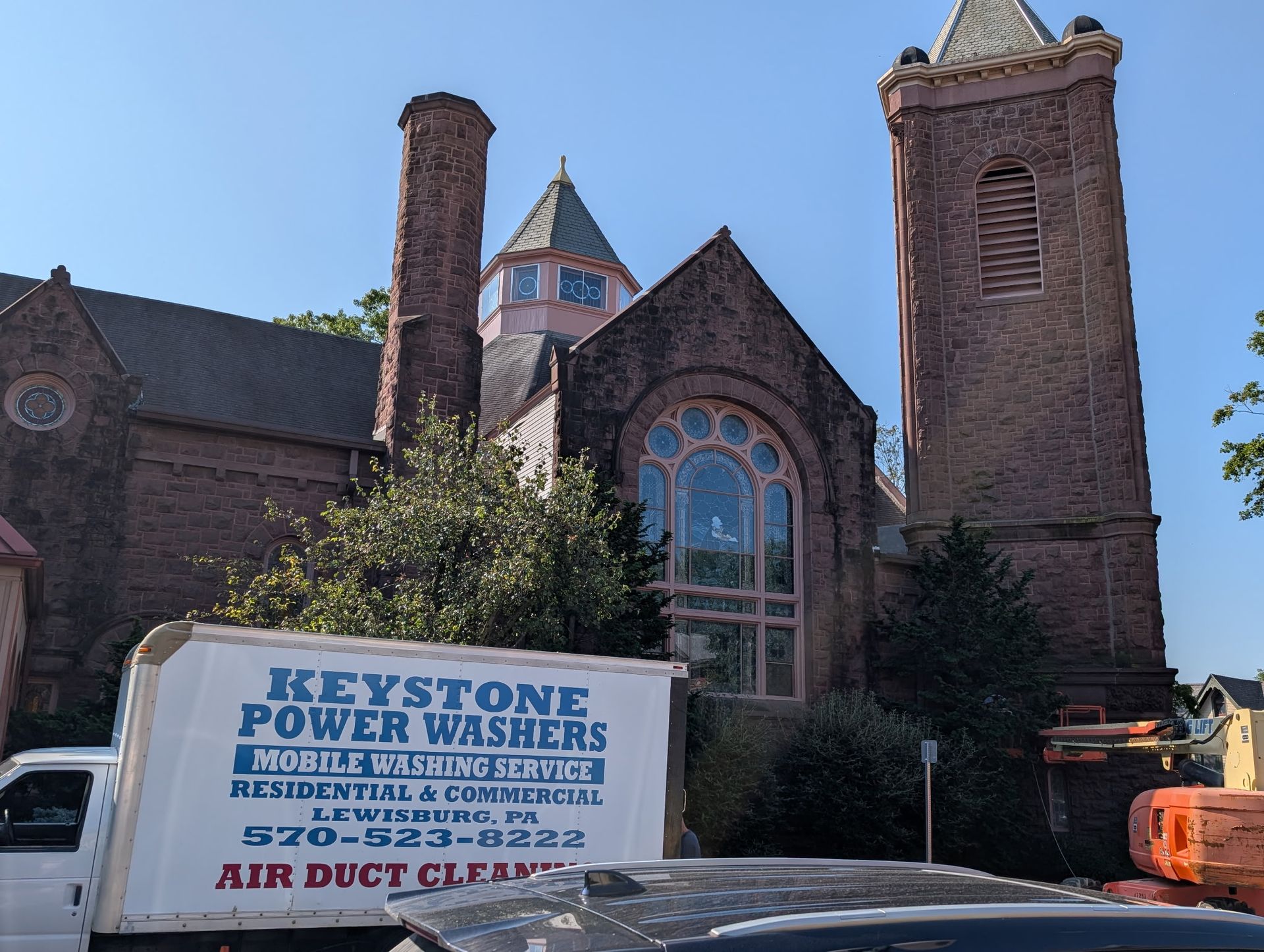 Stone church with arched windows, a power-wash truck, and an orange lift outside.