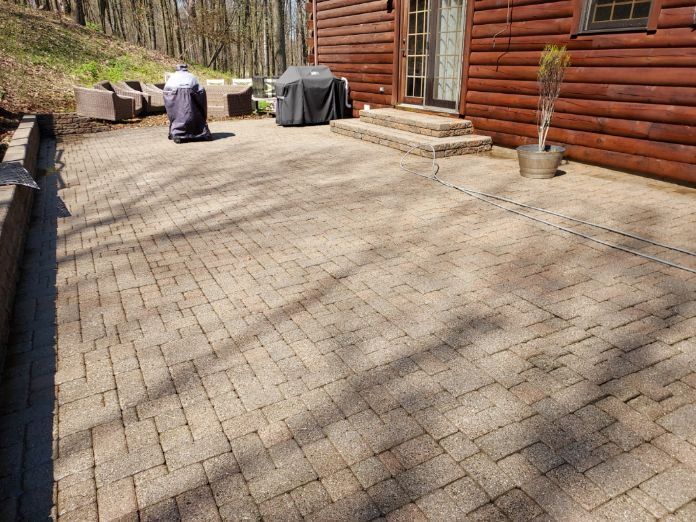 Brick patio beside a wooden house with potted plants and covered outdoor grills