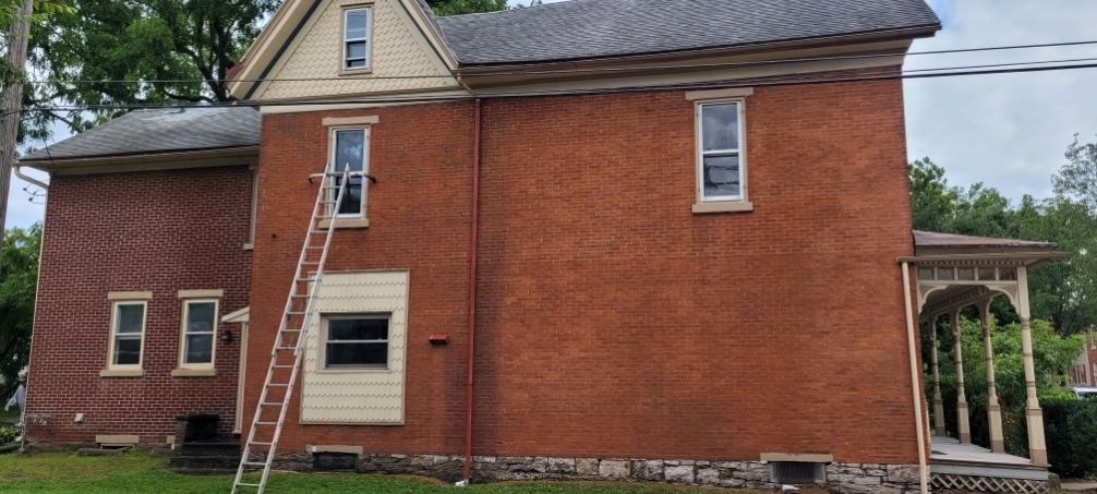 Two-story red brick house with an extension, ladder on the side, and a porch on the right