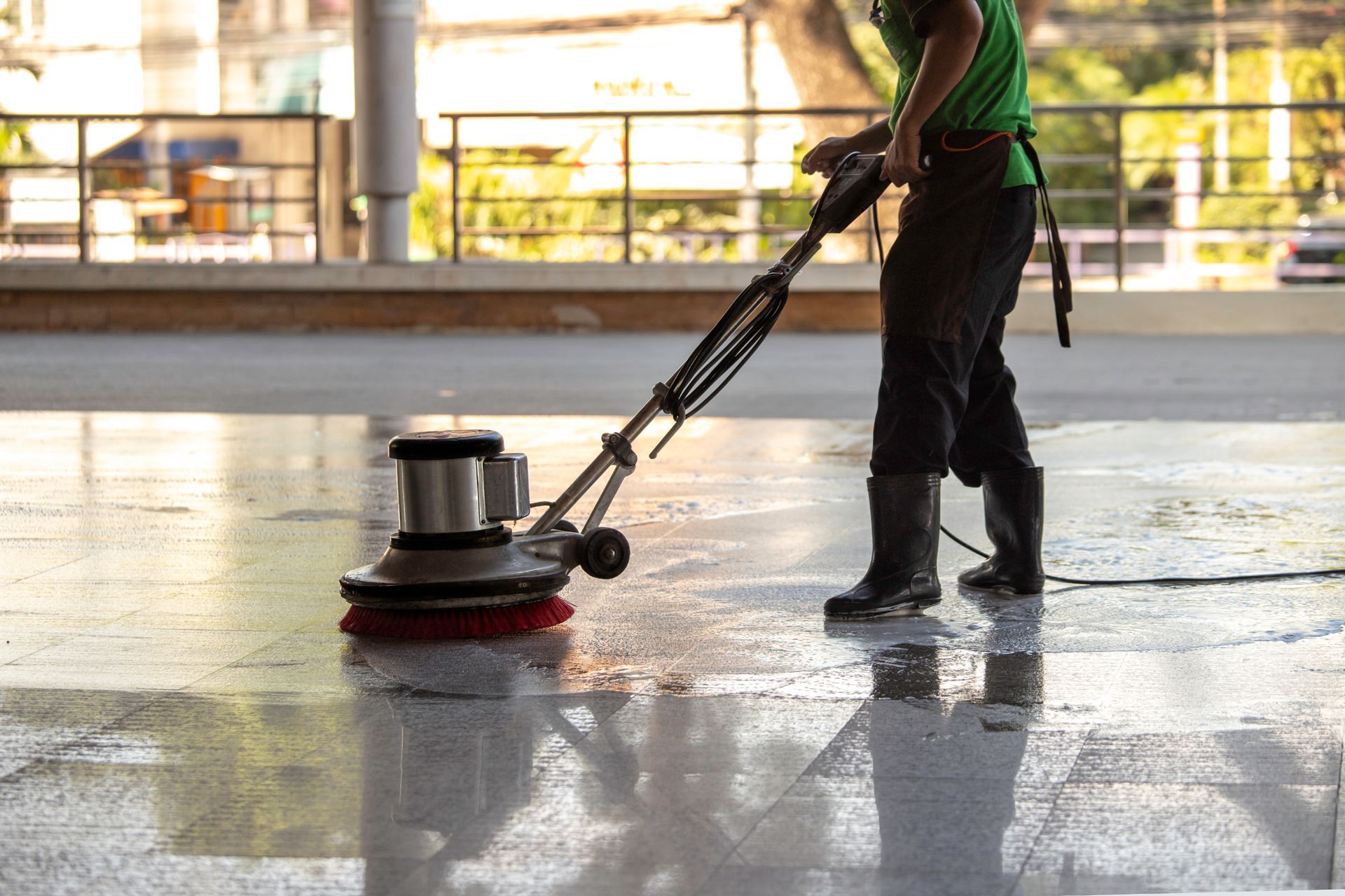 Person cleaning a shiny floor with a floor buffer in a bright indoor space