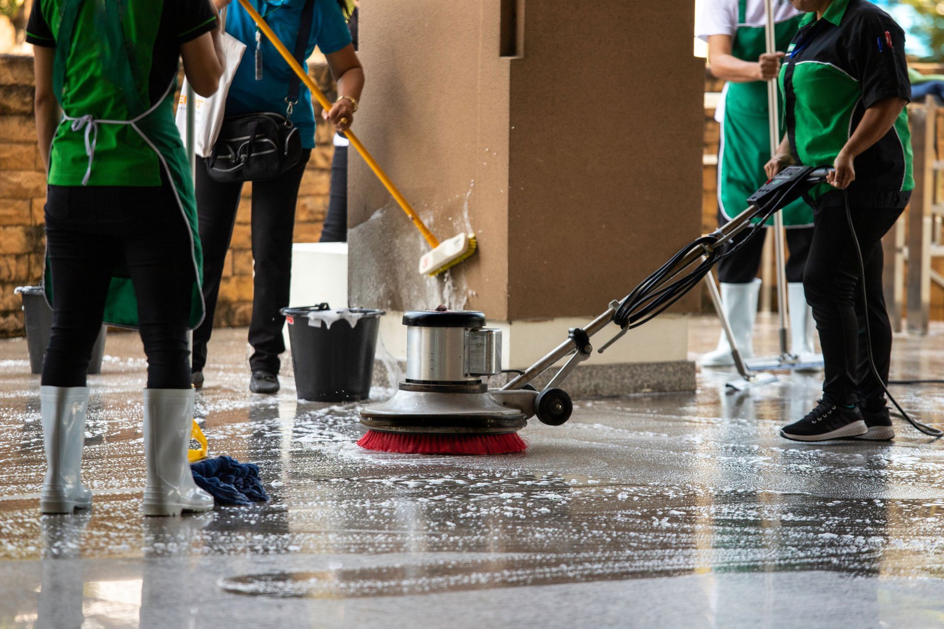 People cleaning a wet floor with mops and a floor scrubber in a building hallway