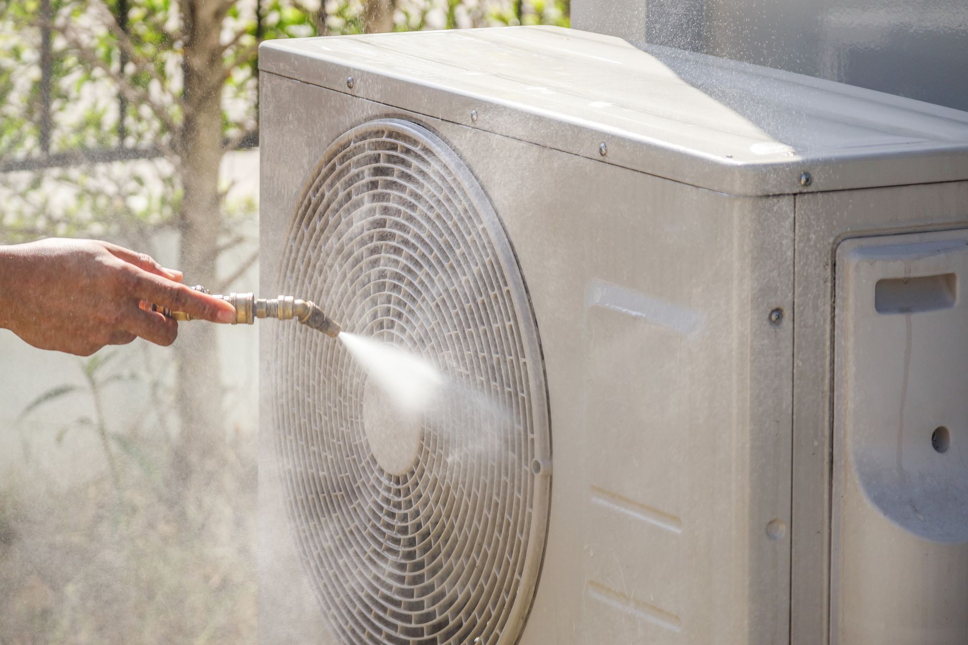 Hand spraying water onto an outdoor air conditioner condenser unit to clean it