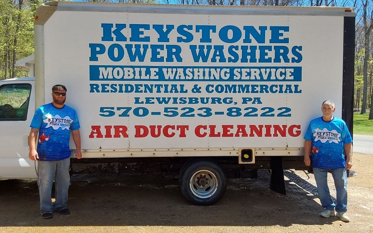 Keystone Power Washers truck with blue logos; two people stand beside it in front of a building.