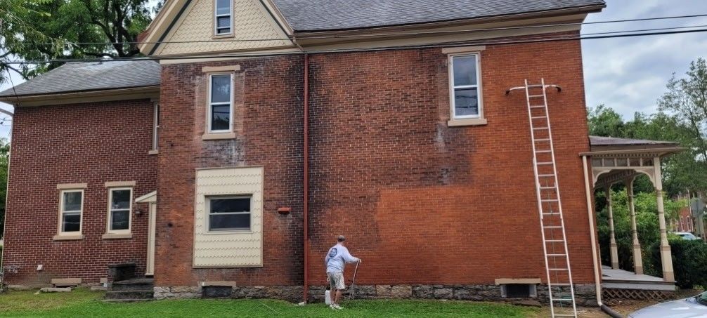 Red brick house exterior with a white-trimmed porch and a person mowing the lawn.