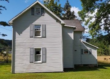 White farmhouse with gray shutters and an attached side wing on a sunny green lawn
