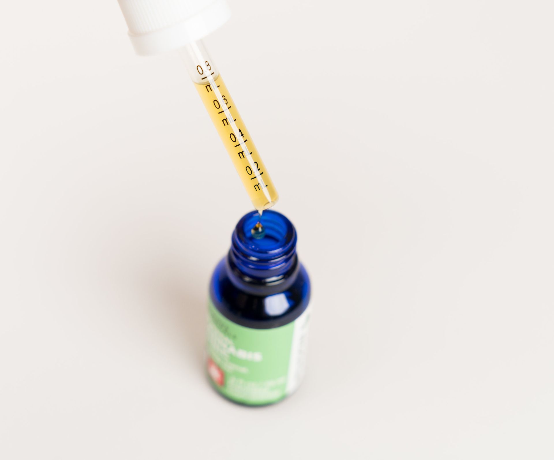 Yellow dropper hovering over an open blue bottle on a white background
