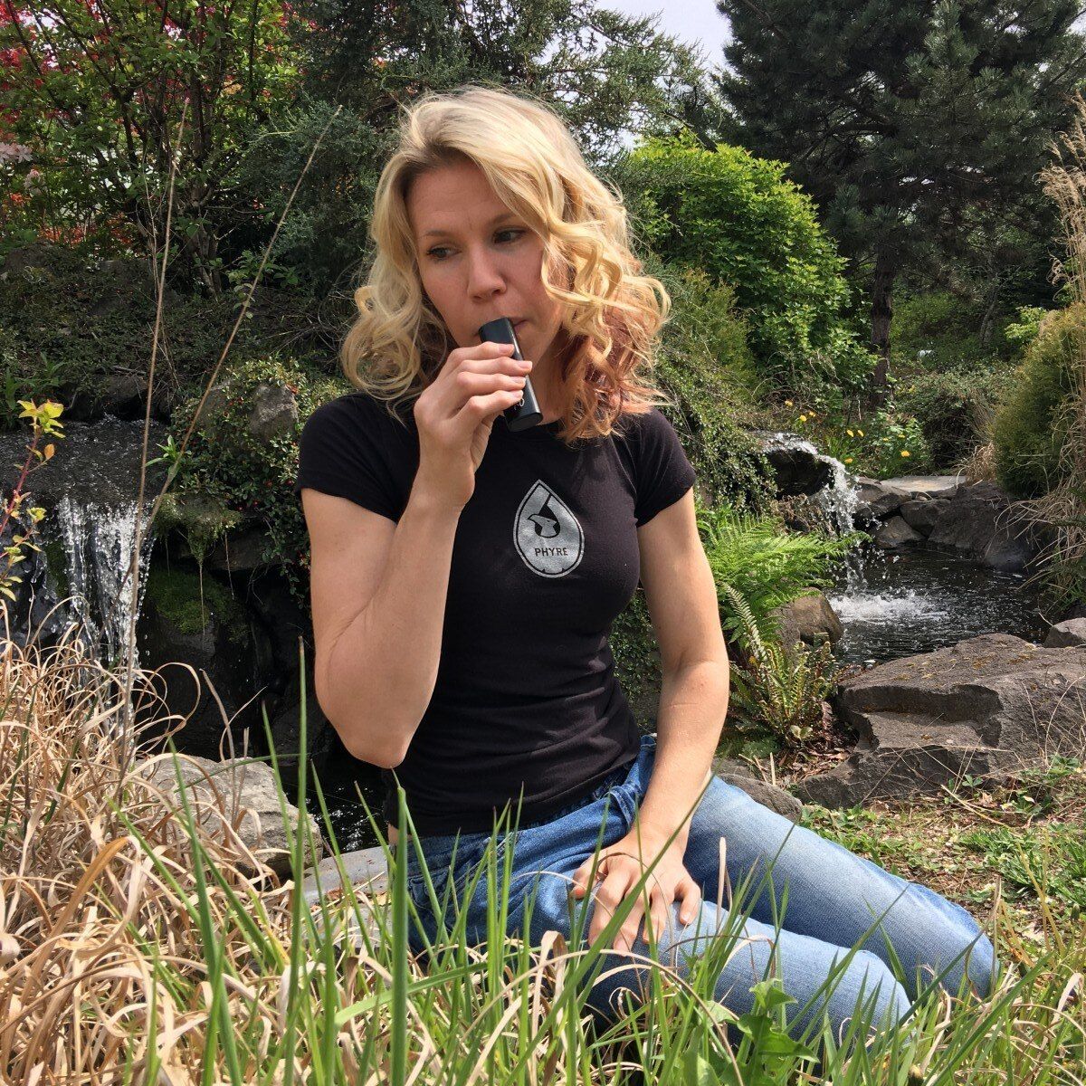 Woman kneeling in grass and blowing a whistle near a garden pond and rocks