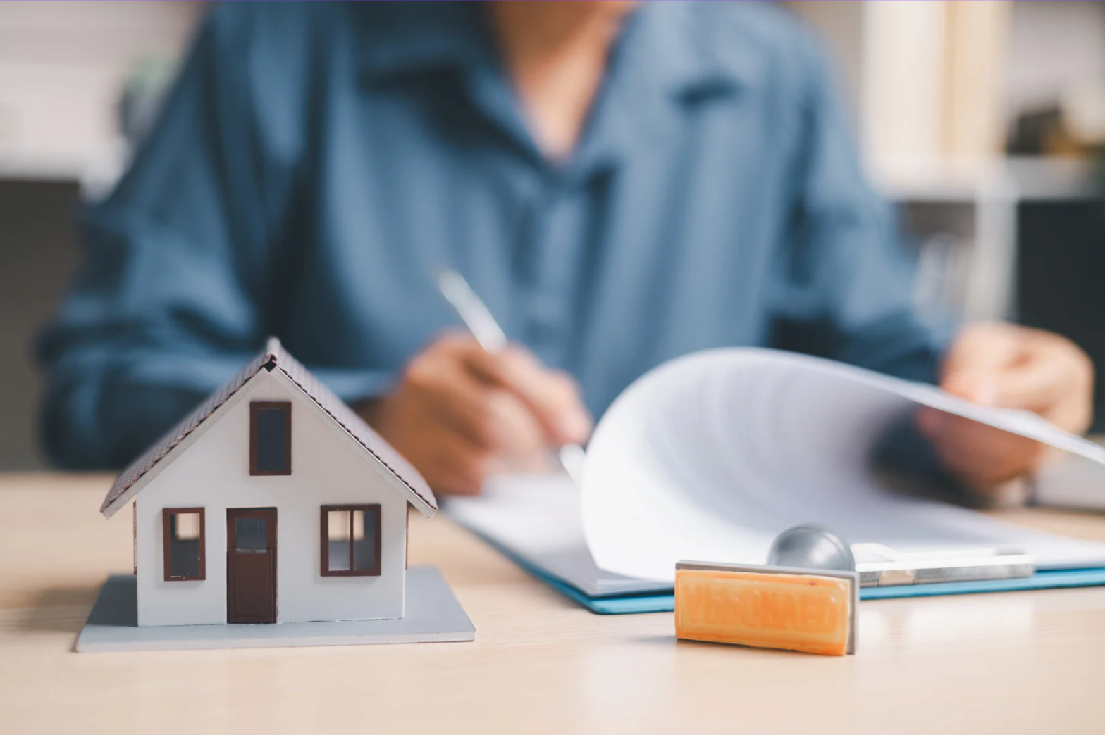 Person reviewing rental property documents with a wooden house model on a desk.