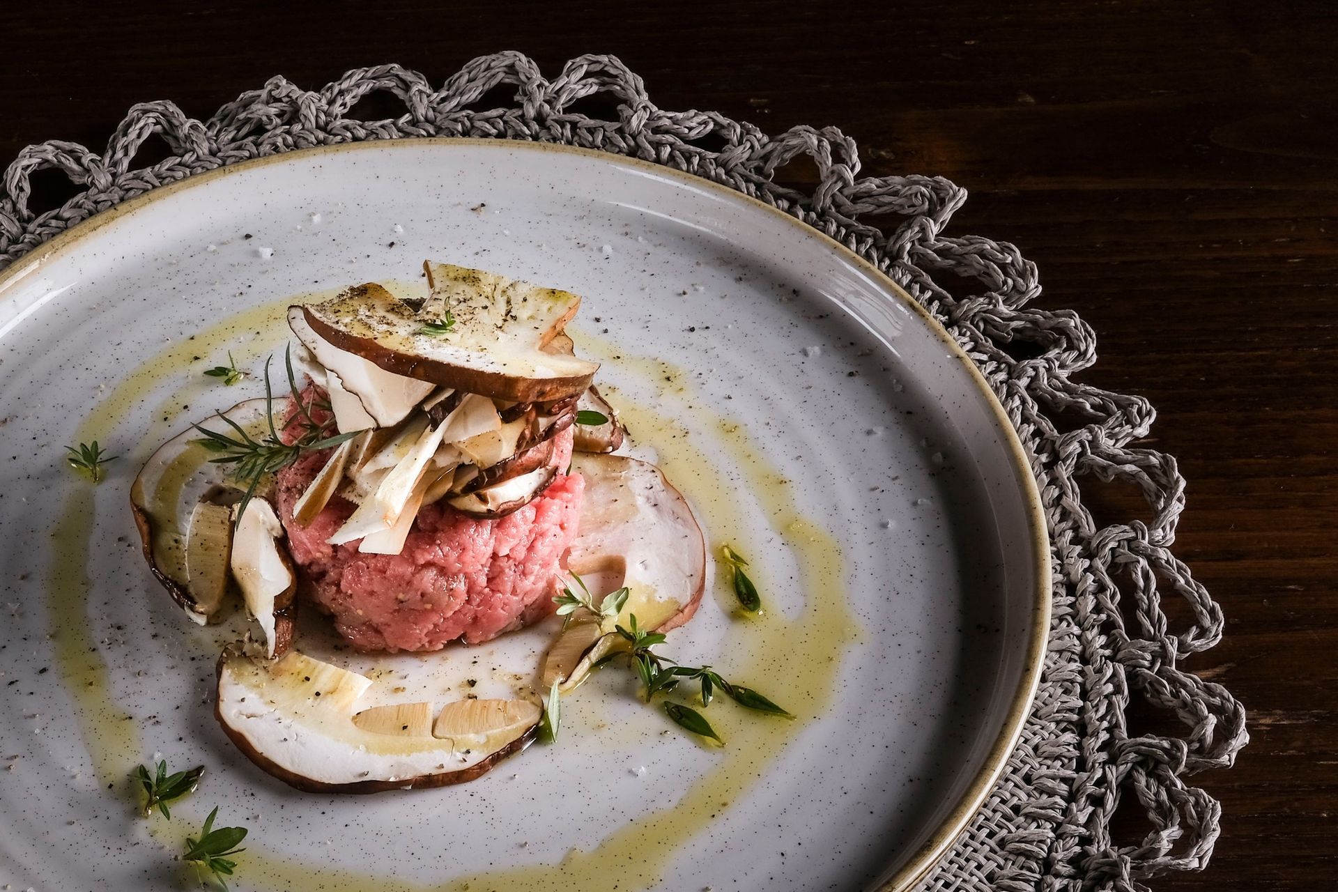 Una porzione di tartare di manzo guarnita con funghi tagliati a fettine sottili e erbe aromatiche