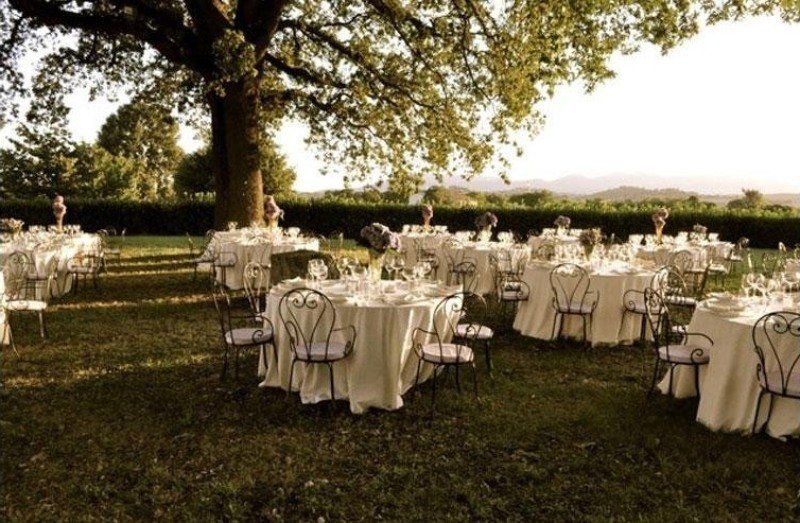 Tavoli e sedie allestiti per un ricevimento di nozze sotto un albero