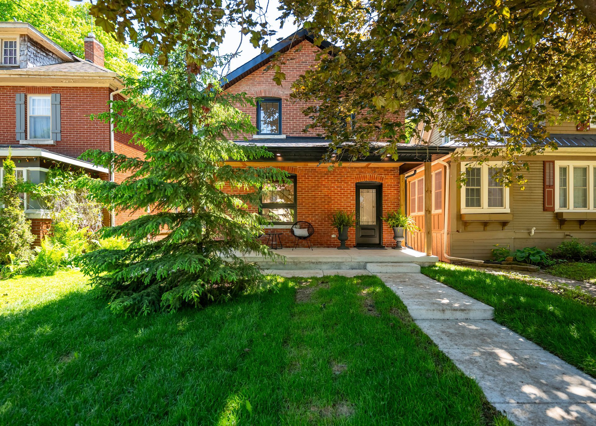 Brick house with green lawn, trees, and a concrete walkway on a sunny day.
